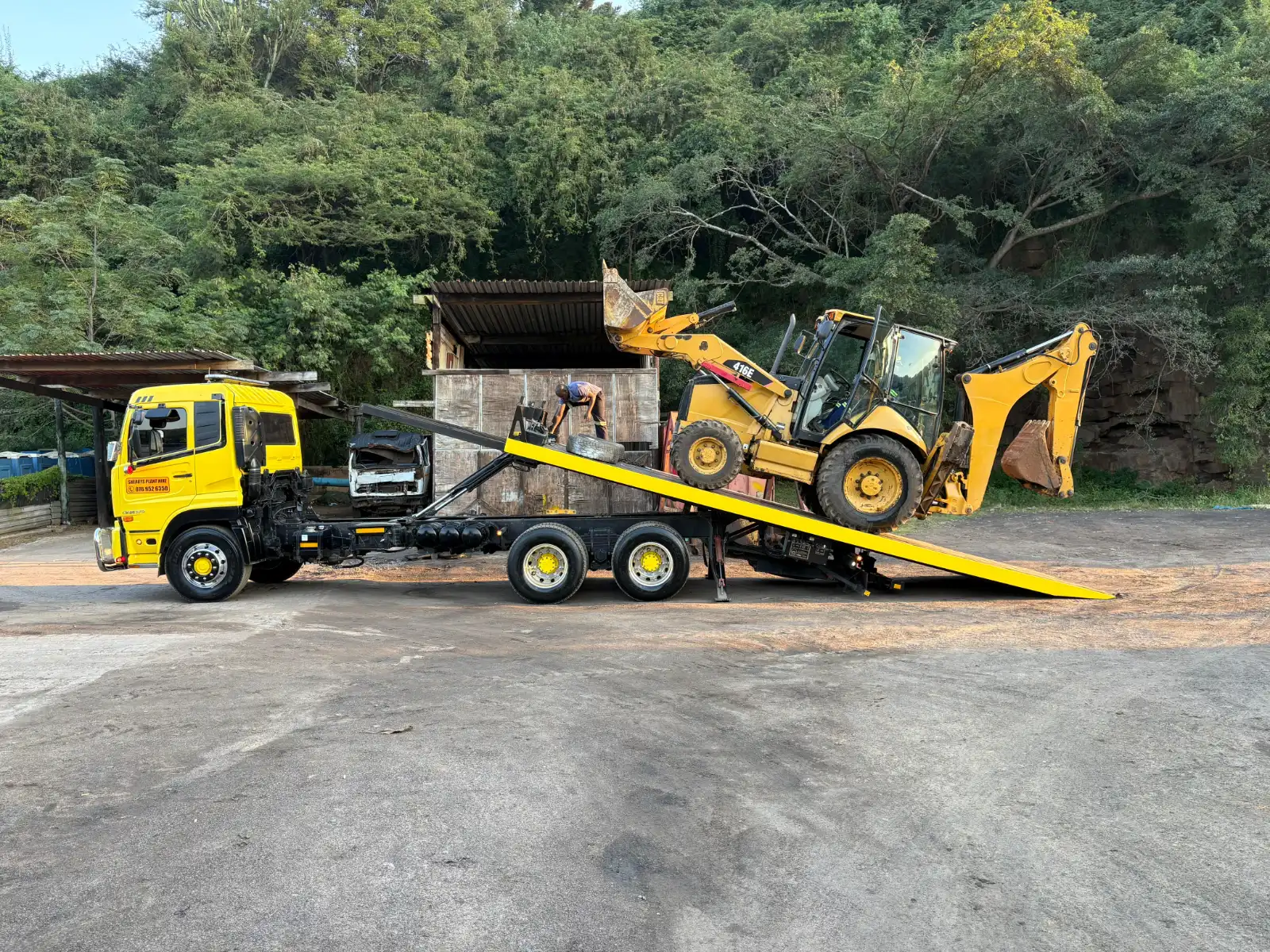 A CAT 416E TLB being driven up the ramp onto one of Sherry's yellow rollbacks