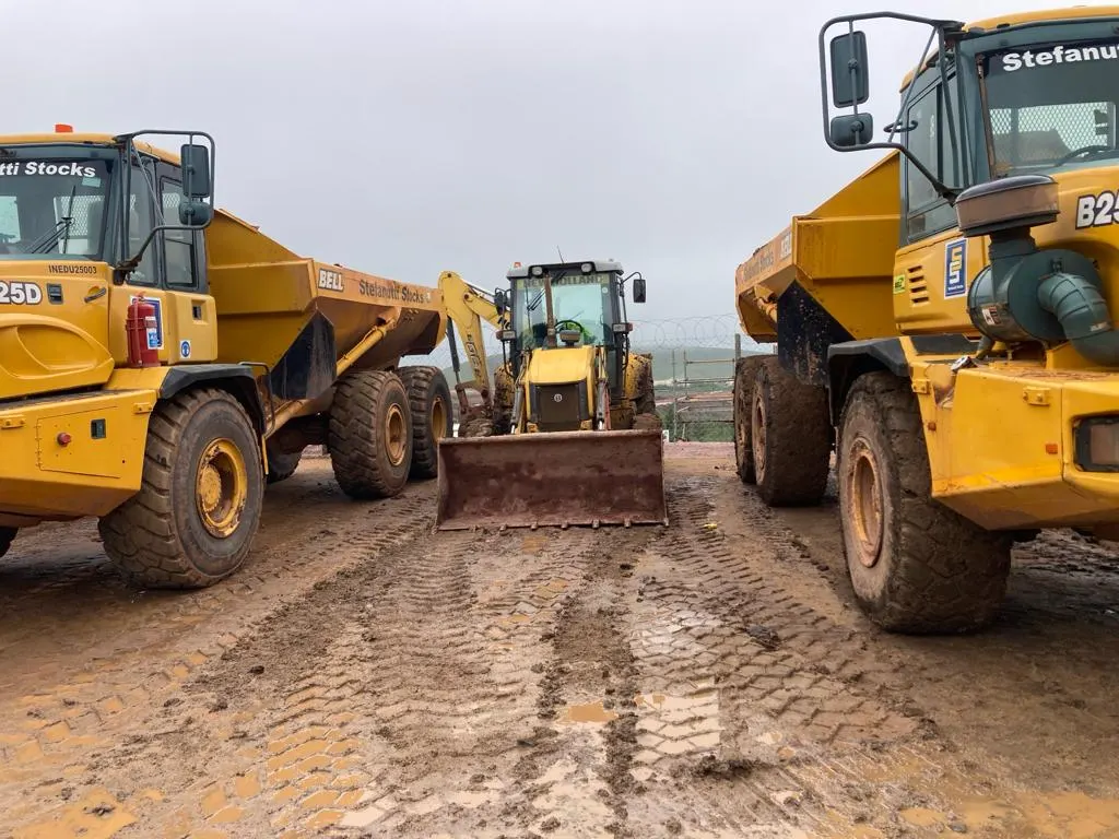 Sherry's TLB working between two articulated dump trucks on a wet site platform
