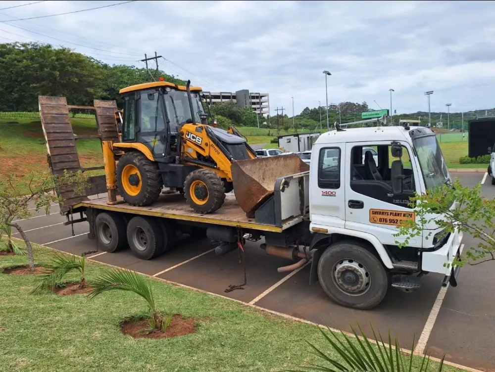 A JCB TLB loaded on Sherry's flatbed truck with the ramps stowed